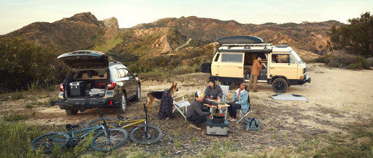 A group of friends gather around a camping table and prepare food