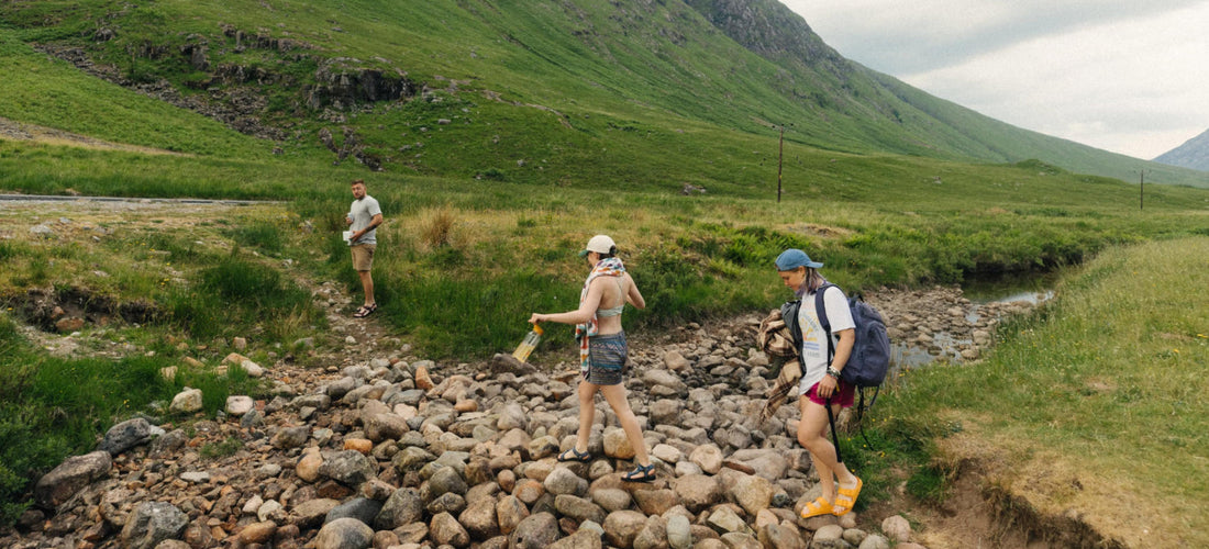 A group of friends walk through a dry river carrying camping gear