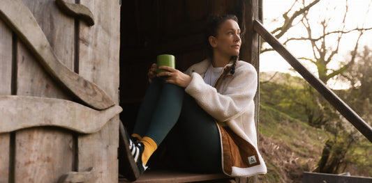 Lise Wortley sits in a cabin doorway holding a flask of coffee
