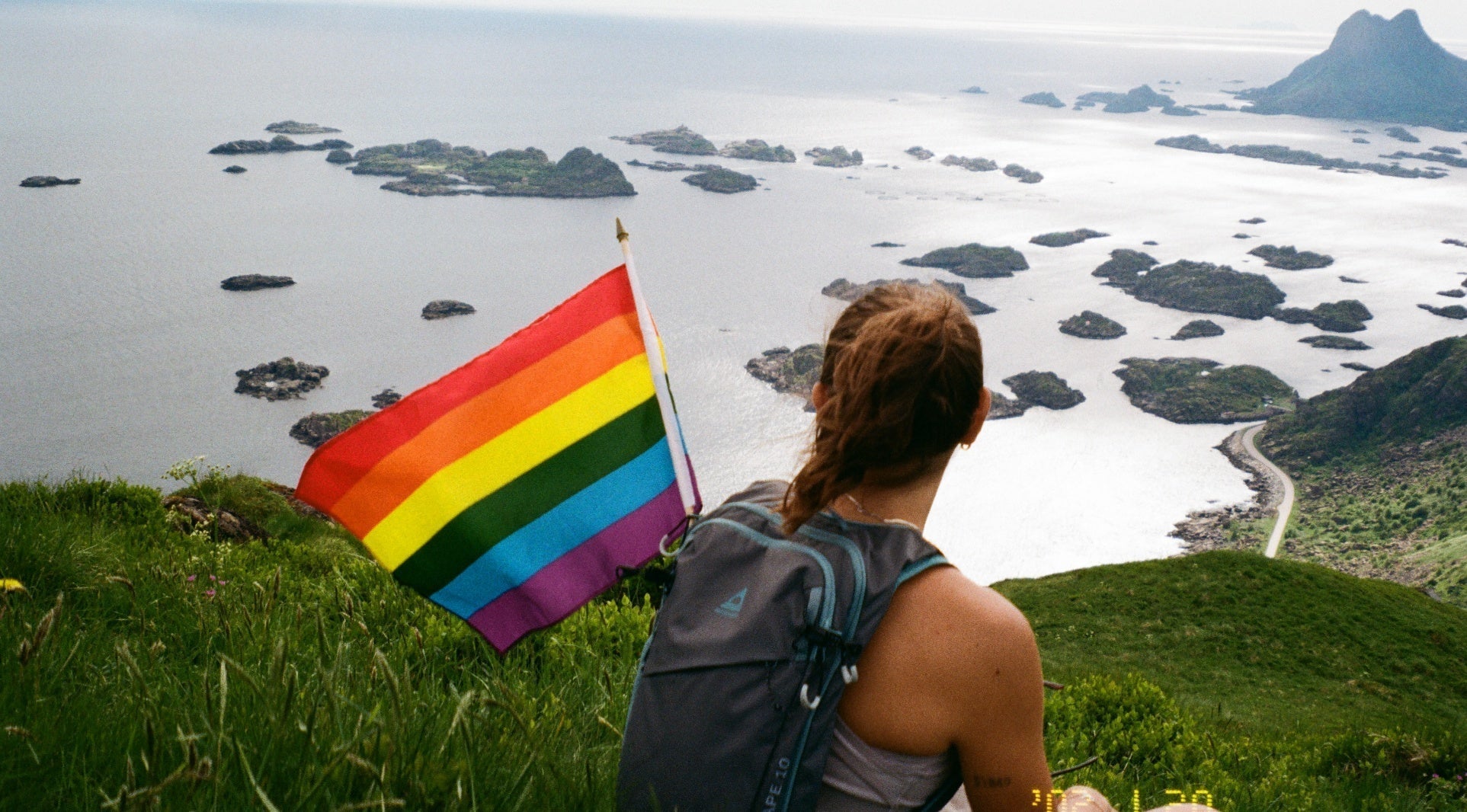 Woman holding a rainbow flag overlooking a bay with small islands